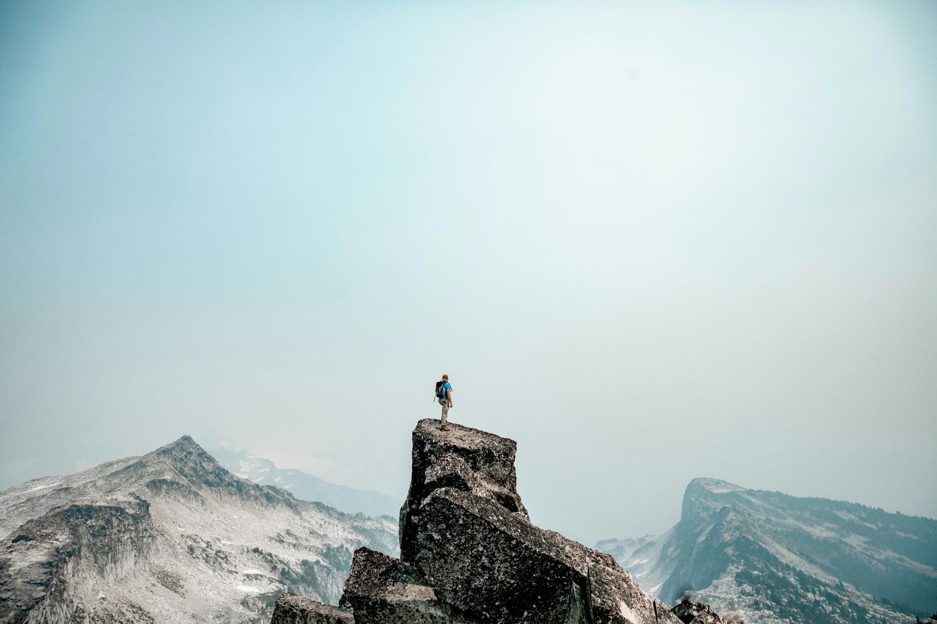 A mountaineer standing on a rocky summit above a mountain range