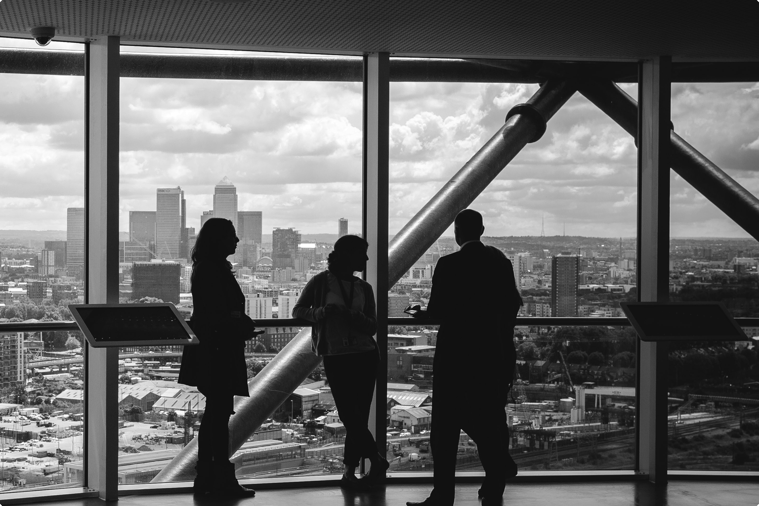 Three professionals in silhouette looking out over a city skyline from a high-rise vantage point